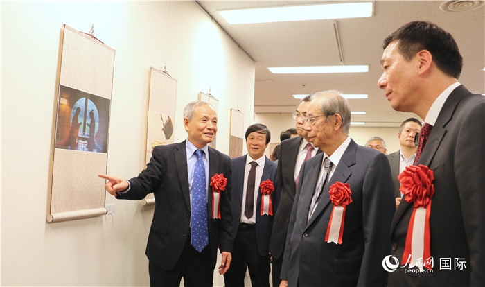 “湖州印象”攝影展主創(chuàng)、世界華人攝影協(xié)會副會長馮學(xué)敏向吳江浩大使、福田康夫前首相等嘉賓介紹展出作品。（人民網(wǎng) 許可攝）