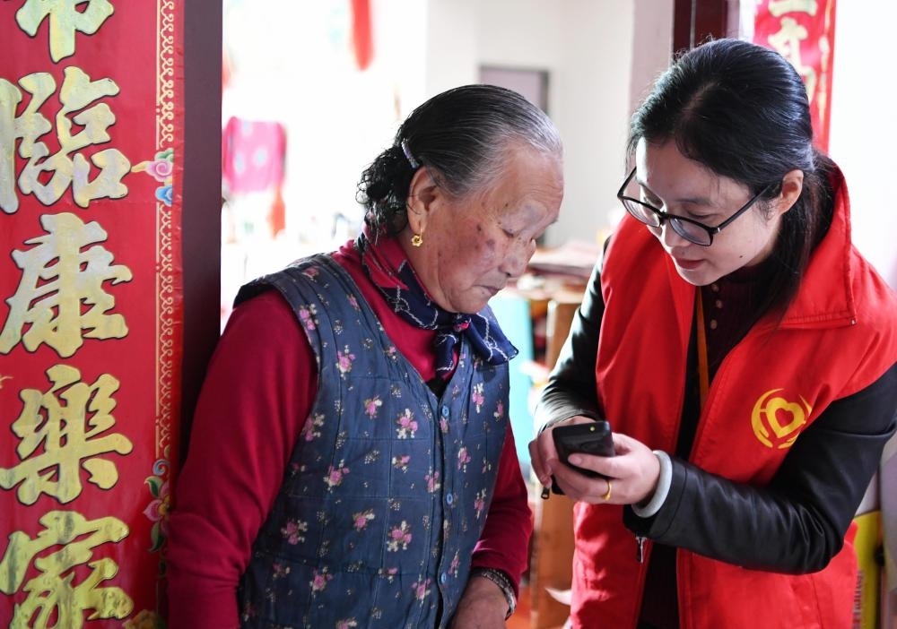 在福州市長樂區(qū)航城街道籌岐村，智慧養(yǎng)老平臺派駐社區(qū)的助老員（右）在為老人陳鳳英（左）講解養(yǎng)老定制手機(jī)的用法（2021年11月26日攝）。新華社記者 魏培全 攝