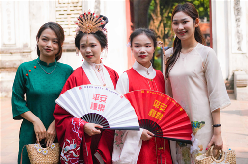身穿古裝的中國游客和身穿越南傳統(tǒng)服飾奧黛的越南青年在文廟門前合影。