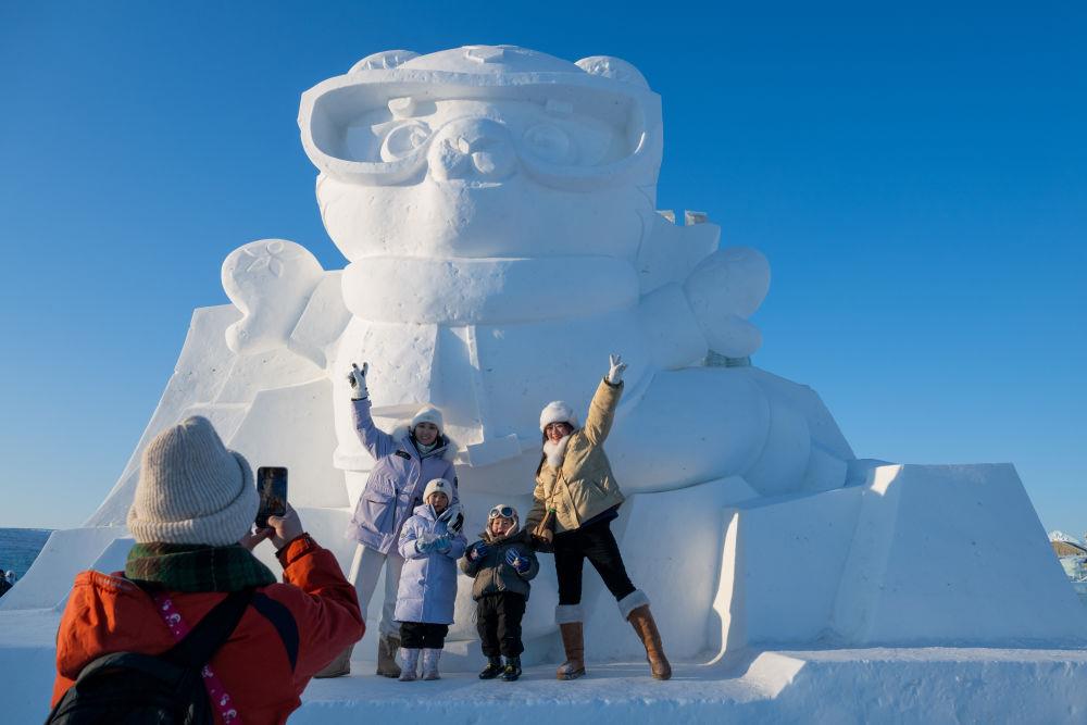 2025年1月3日，在黑龍江哈爾濱冰雪大世界園區(qū)，游客與亞冬會吉祥物雪雕“濱濱”合影